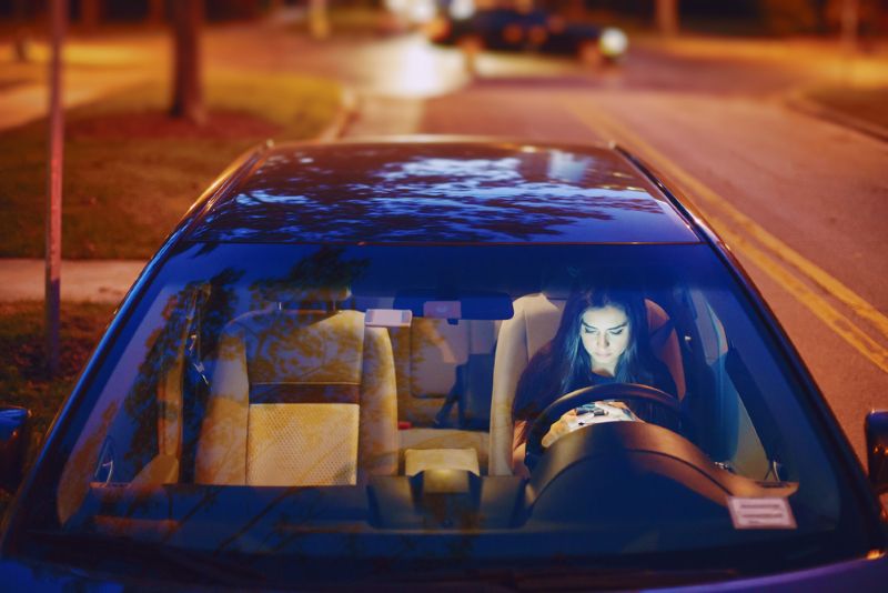 woman pulled over on the side of the road at night looking at her phone