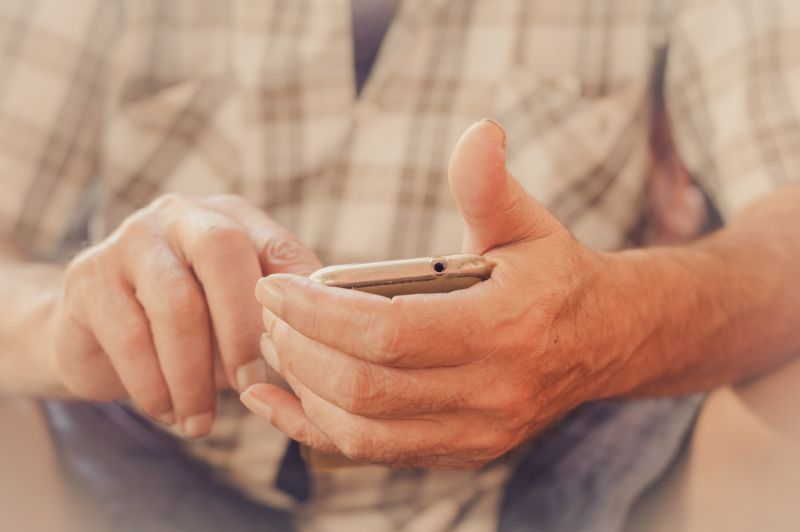 Old man sitting down and typing on his cell phone